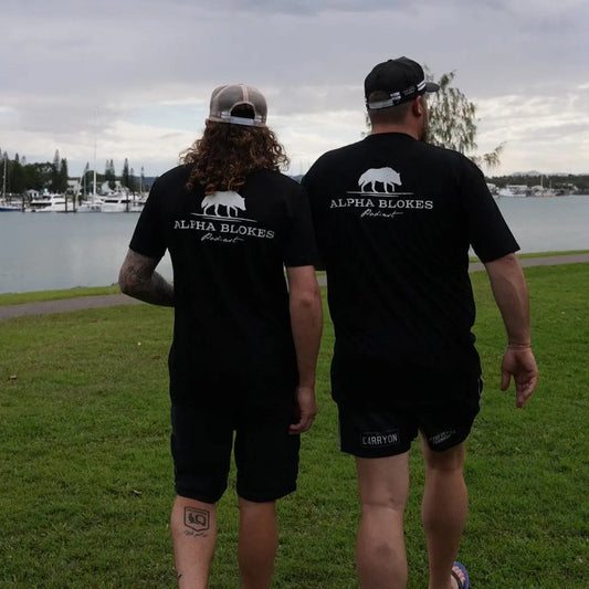 Two people wearing black t-shirts with a logo on a grassy area by a lake.