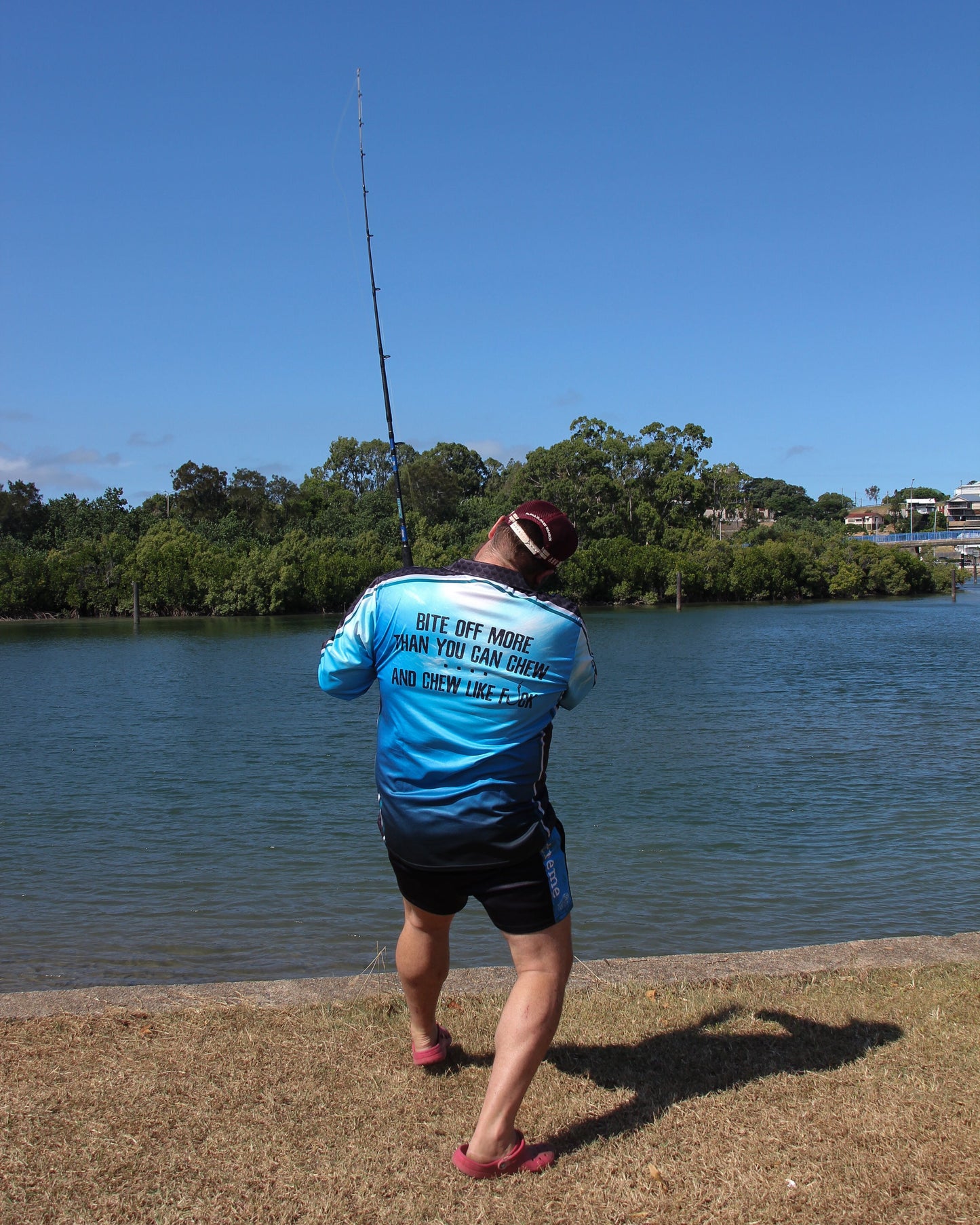 Person fishing by a body of water with trees and a clear sky in the background