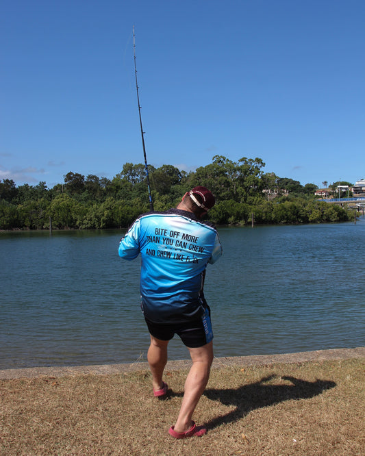 Person fishing by a body of water with trees and a clear sky in the background