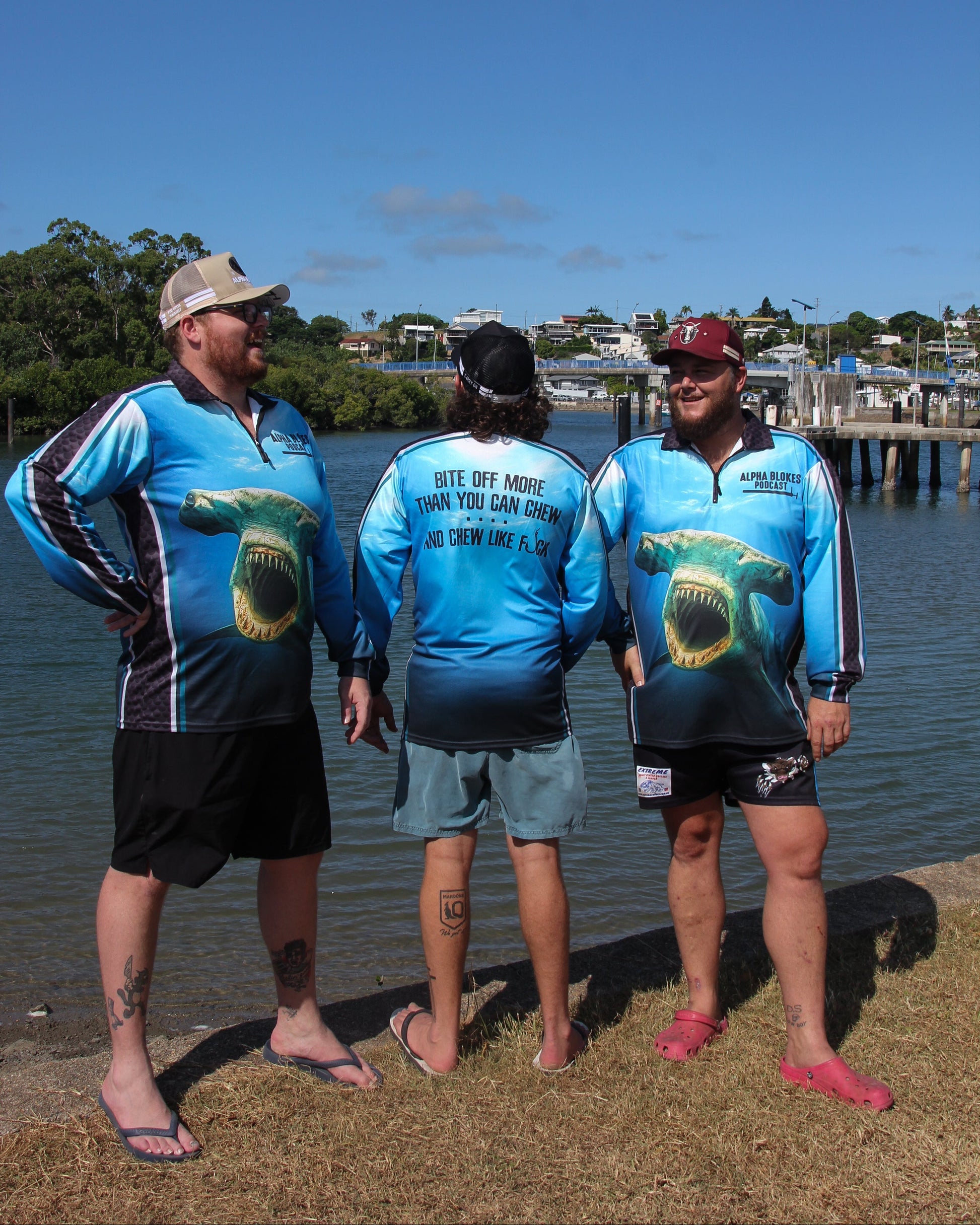 Three men wearing matching blue shirts with a logo by a body of water.