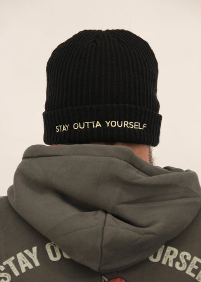 Person wearing a black beanie with 'Stay Outta Yourself' text and a matching jacket.
